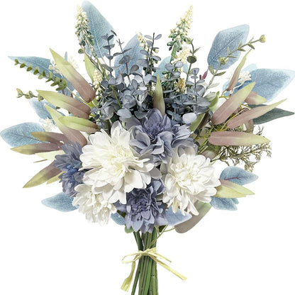 An artificial floral bouquet with white and blue flowers, dusty blue-green foliage, and muted beige leaves, tied with a light yellow ribbon at the stems against a plain white background.