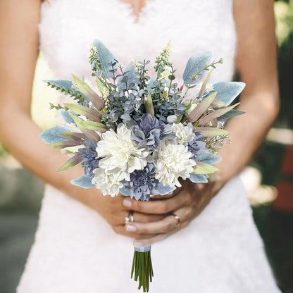 A close-up of a bride in a white wedding dress holding a bridal bouquet with white and blue flowers, blue-green foliage, and green stems.