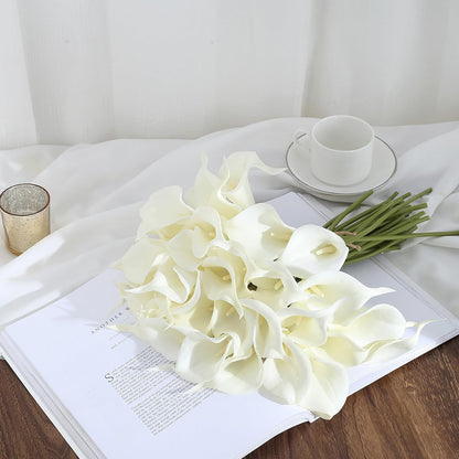 Bouquet of white calla lilies on an open book with a cup and saucer in the background.