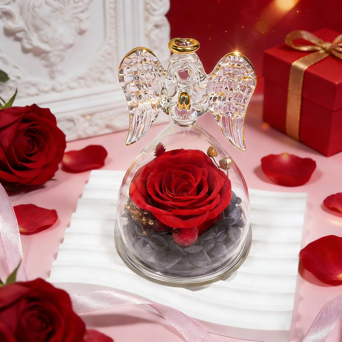Decorative angel figurine with a red rose inside on a pink surface with roses and a gift box.