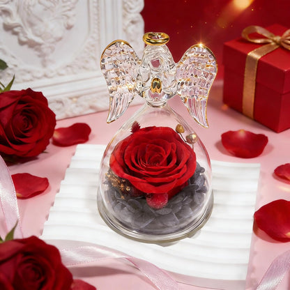 Decorative angel figurine with a red rose inside on a pink surface with roses and a gift box.