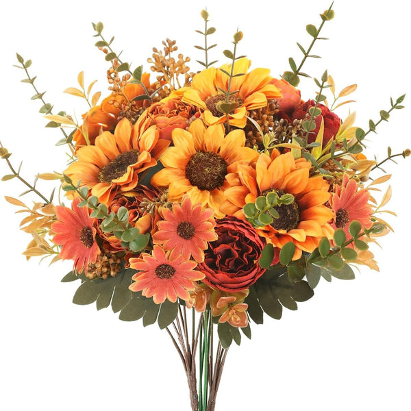 An artificial autumn flower bouquet featuring large yellow and orange sunflowers, coral daisies, dark red peony-style blooms, and green foliage on a plain white background.
